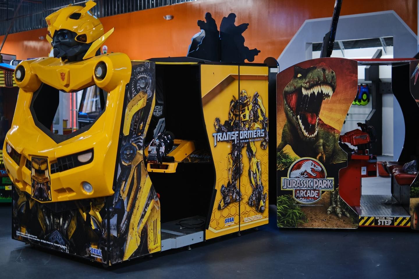 a Transformers arcade game is sitting next to a Jurassic Park arcade game