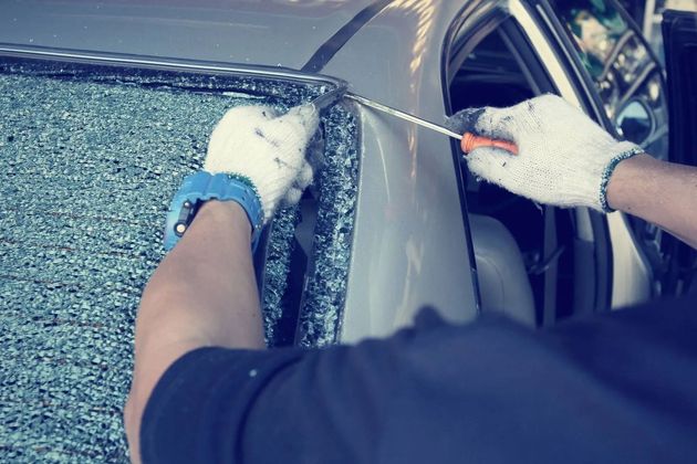 Gloved hands using a scraper to remove ice from a car windshield