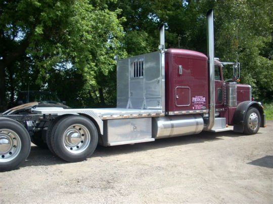 a red semi truck is parked in a dirt lot with trees in the background .