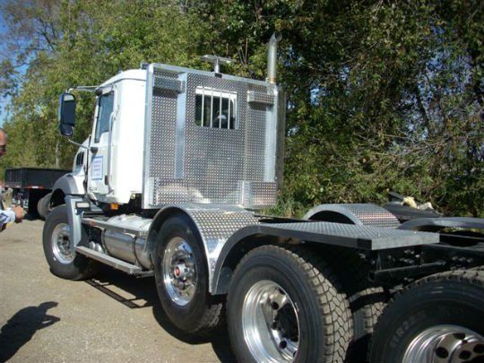 a white semi truck with a cage on the back is parked on the side of the road .