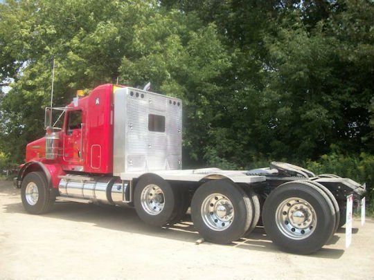 a red semi truck is parked in a dirt lot with trees in the background .