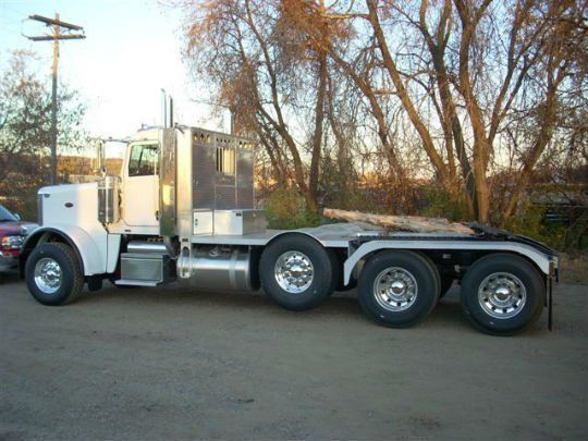 a white semi truck is parked in a parking lot with trees in the background