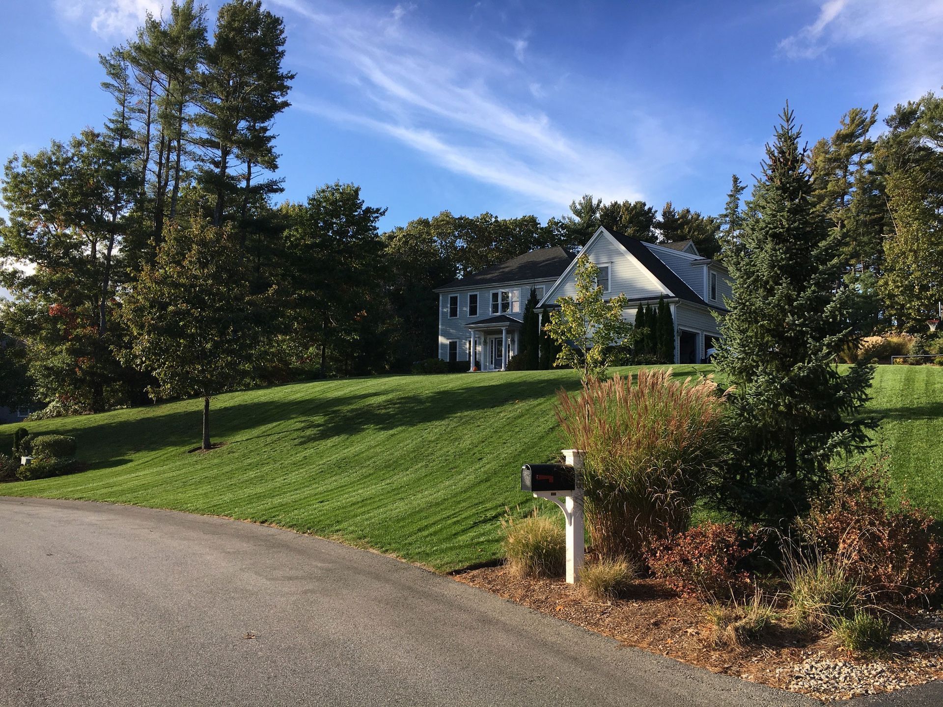 A large white house sits on a lush green hillside next to a mailbox