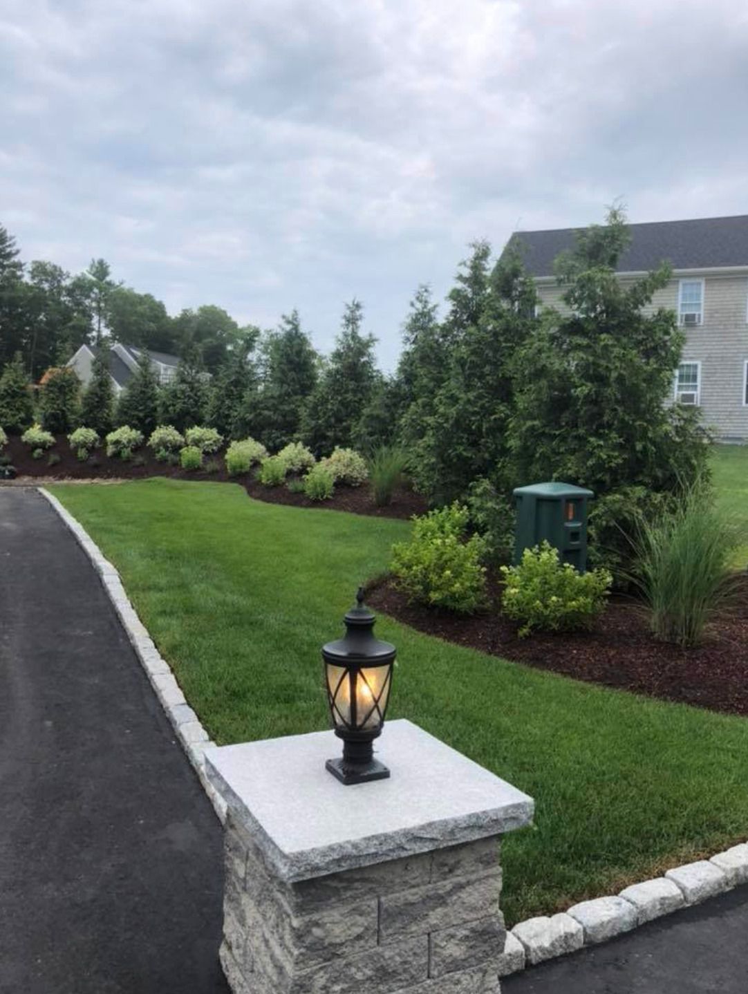 A lantern is sitting on top of a stone pillar next to a driveway