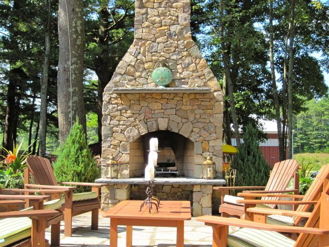A stone fireplace is surrounded by chairs and a table