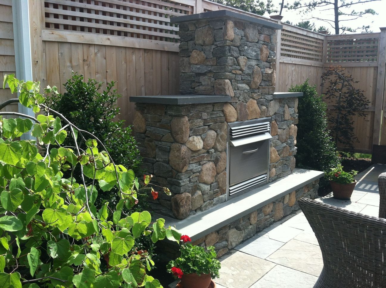 A stone fireplace is sitting on a patio next to a wooden fence