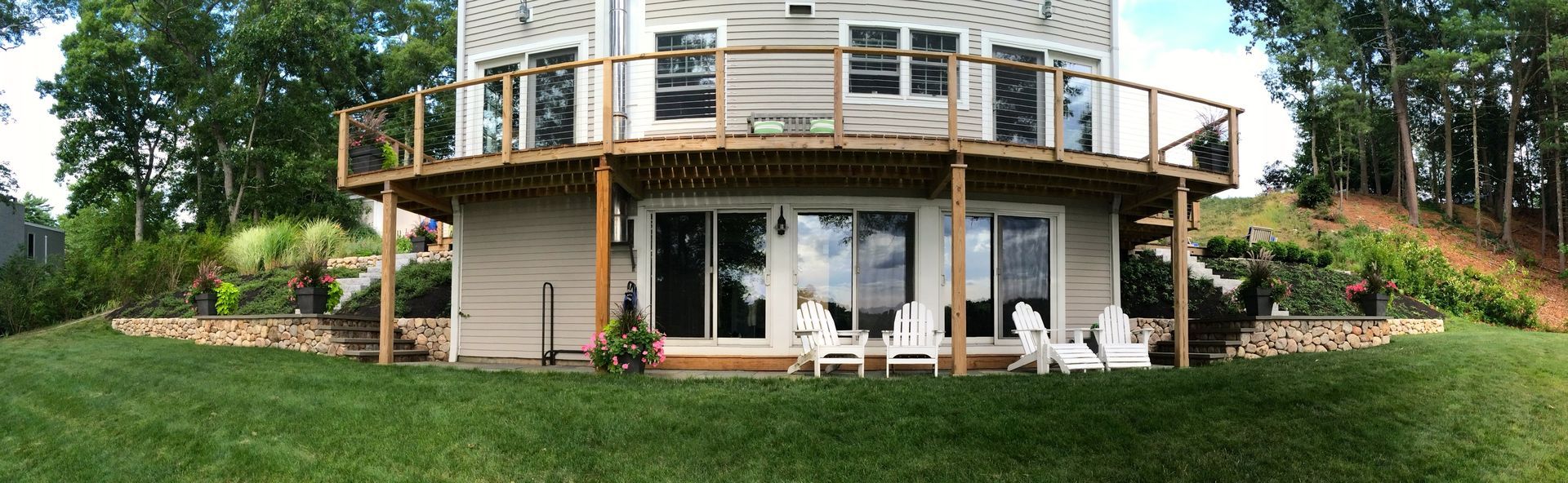 A large house with a large deck is sitting on top of a grass covered hill