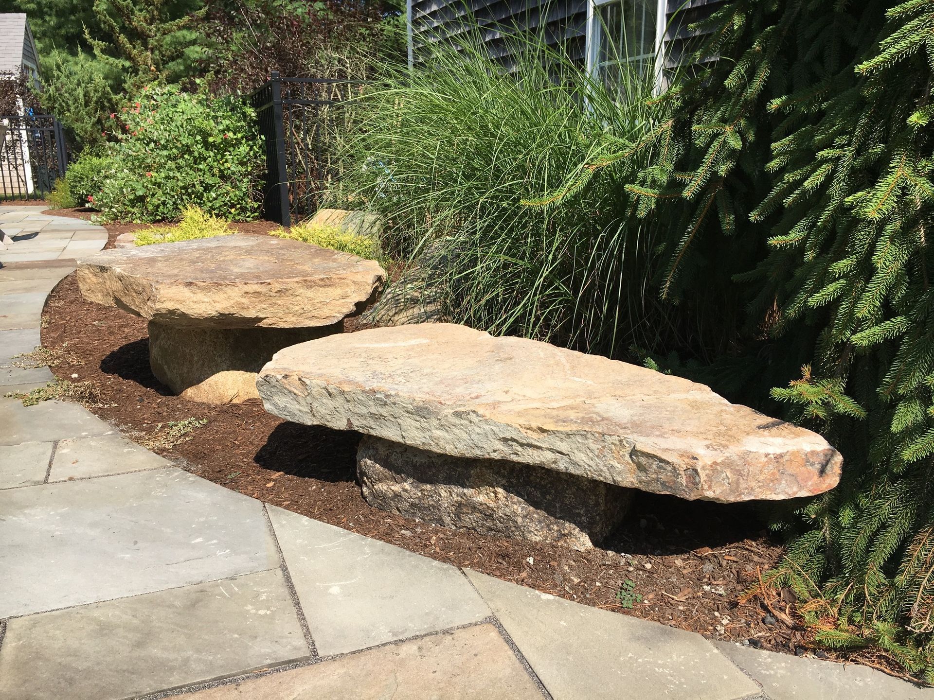 A stone bench is sitting on a patio next to a bush