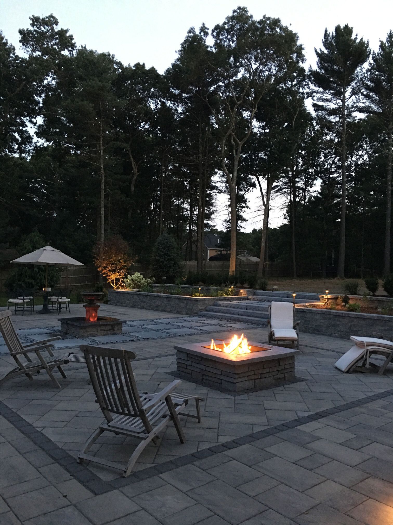 A fire pit on a patio with chairs and umbrellas