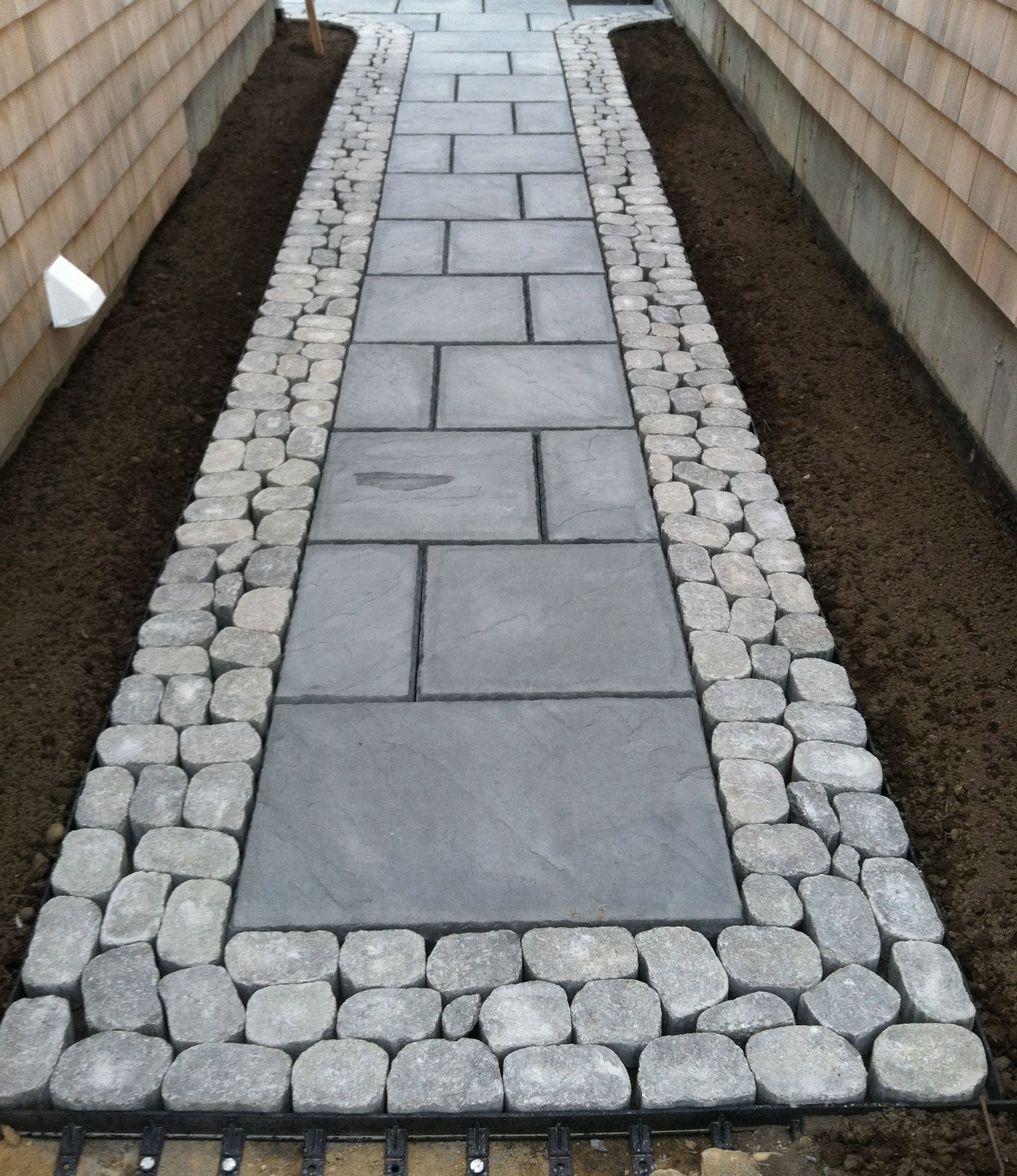 A stone walkway between two buildings with a light on the side