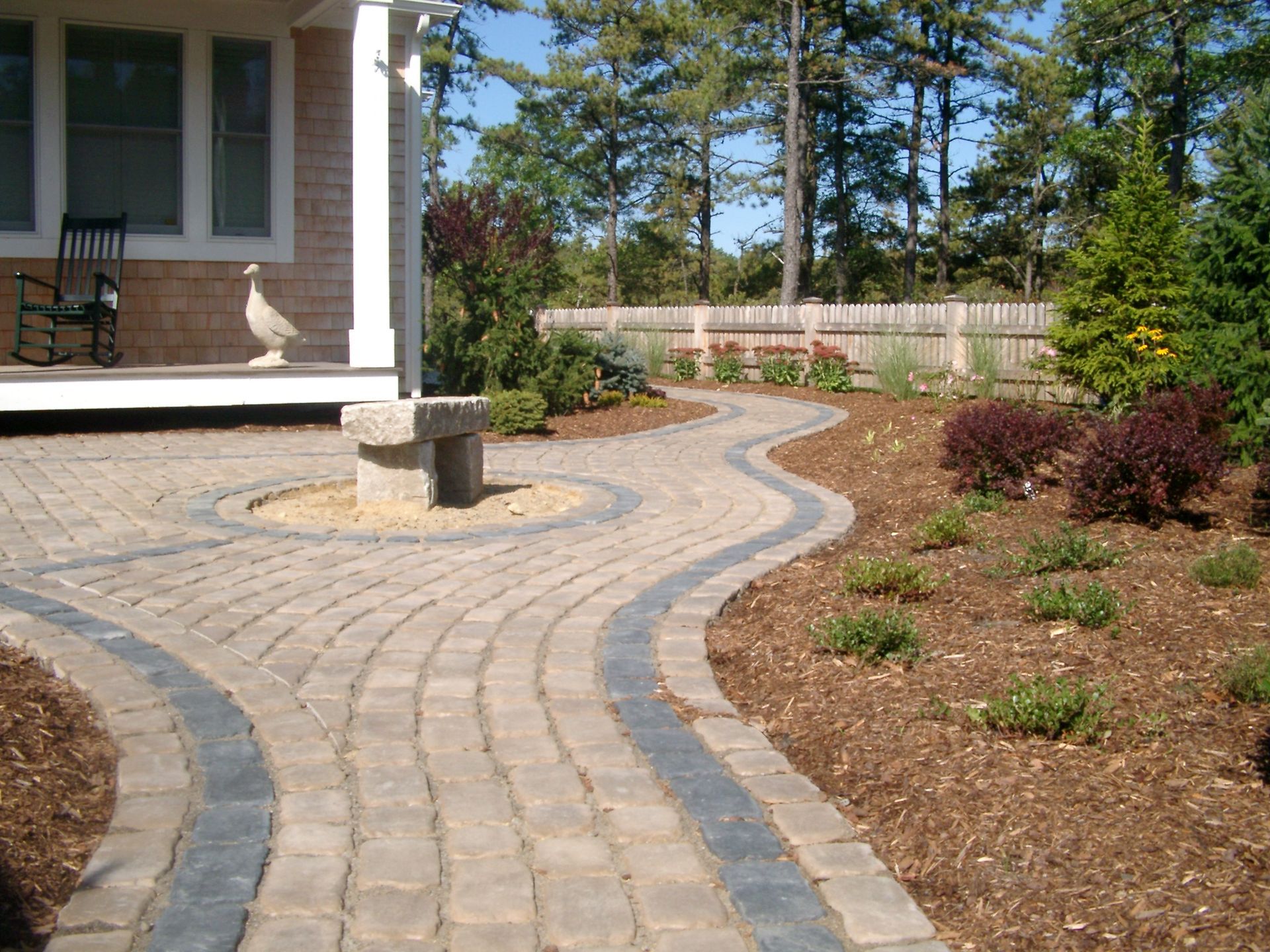 A brick walkway leading to a porch with a rocking chair