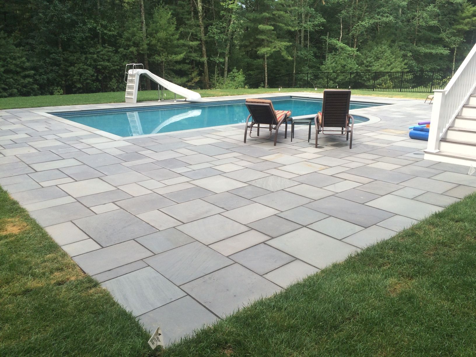 A patio with chairs and a swimming pool in the background
