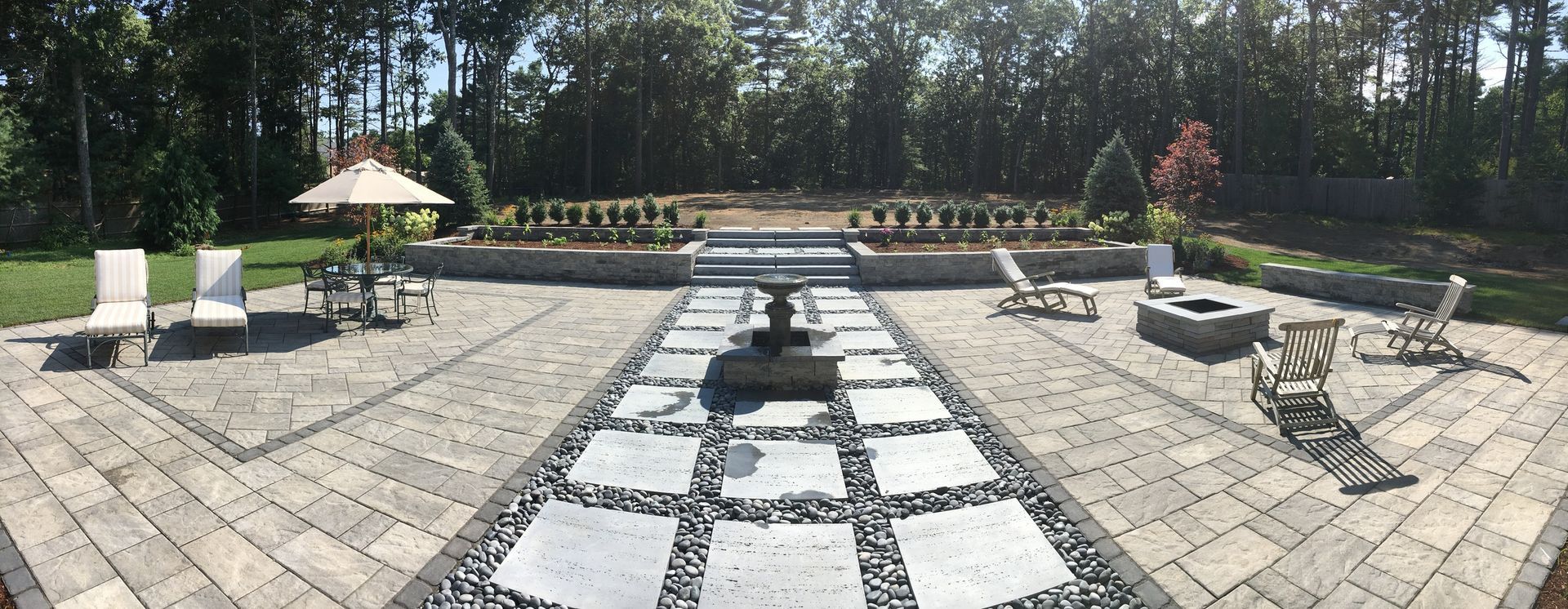 A large patio with a fountain, chairs , umbrellas and a fire pit