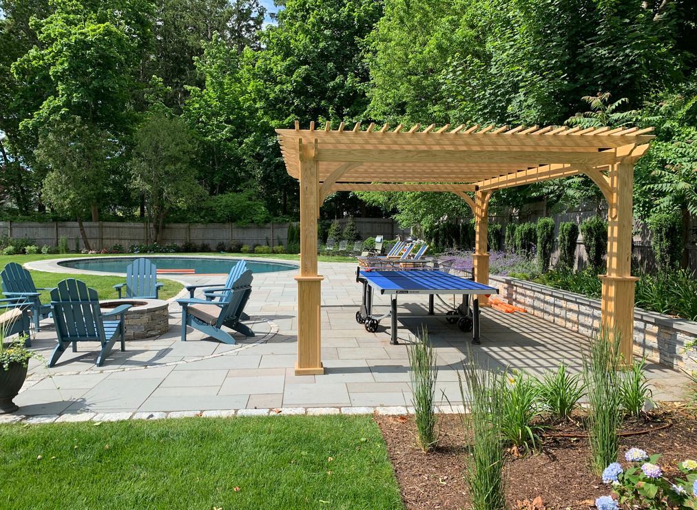 There is a ping pong table under a pergola in the backyard