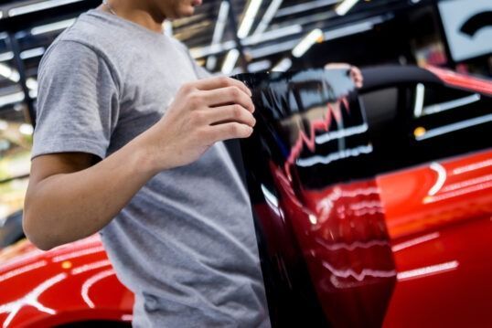 Person holding a red garment beside a red car in a garage