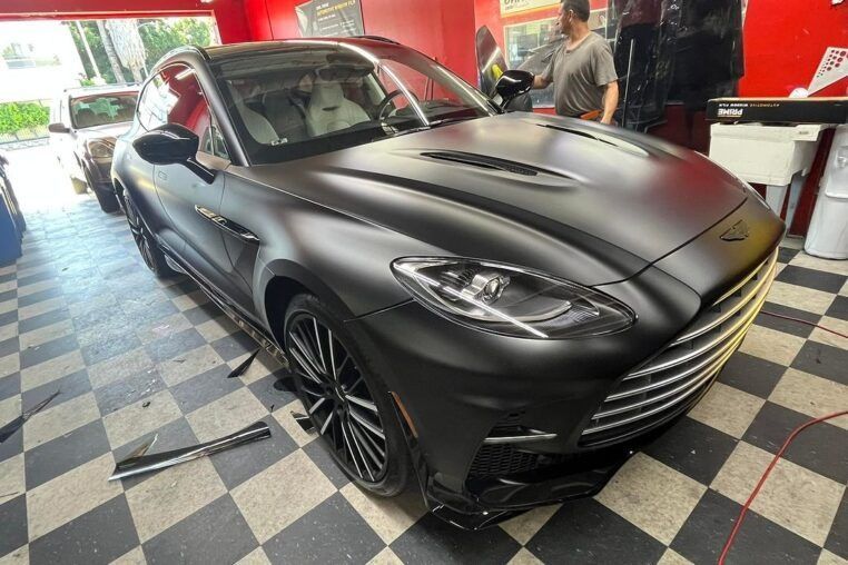 Matte black sports SUV in a garage, with a man standing nearby on a checkered floor.