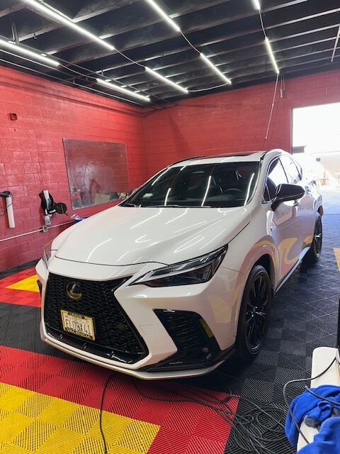 White Lexus SUV in a red auto detail shop with yellow floor mats and bright ceiling lights