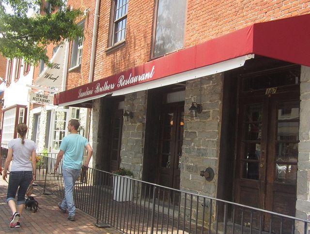 People walking past a brick building with a red awning that reads