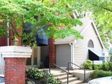 Small beige house with gray garage door, red brick pillar, and tree in front.