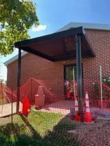 A black awning shelters a brick building entrance. Orange construction cones and fencing block access.