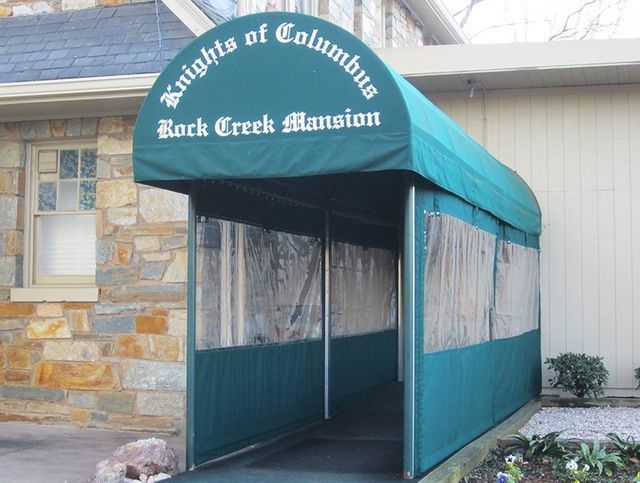 Green awning over entrance to Knights of Columbus building, Rock Creek Mansion. Clear plastic side panels, stone wall.