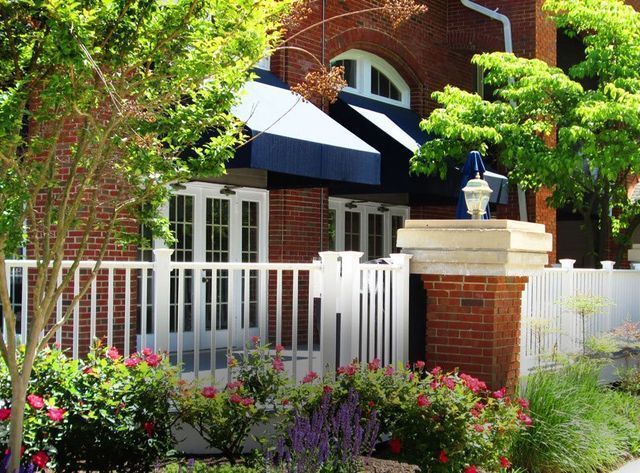 Brick building with white picket fence, awning, and colorful flower beds.