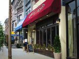 Restaurant with red awning, sidewalk seating, storefront windows, and a chalkboard sign.