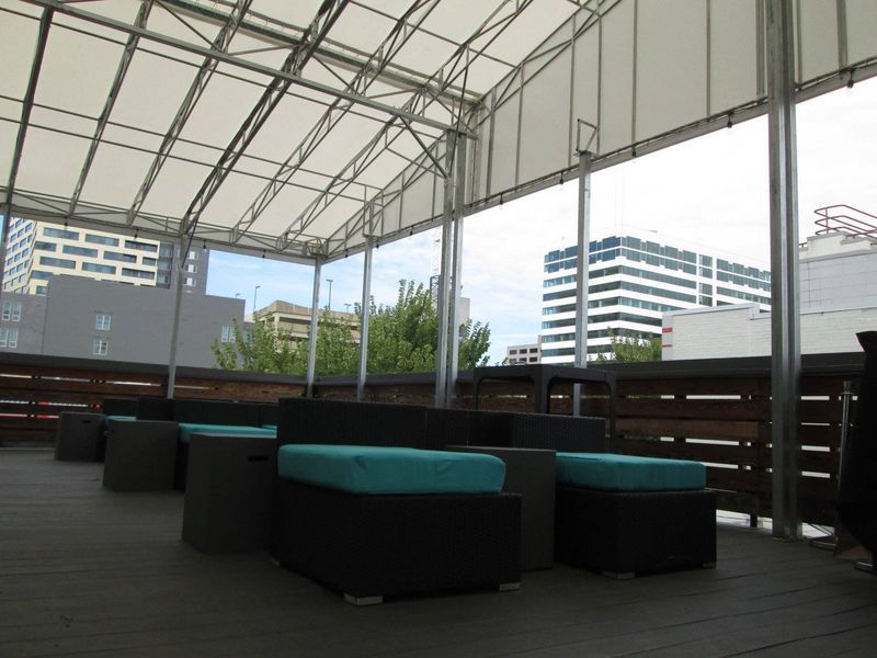 Rooftop lounge with teal cushions, black furniture, and city views under a covered canopy.