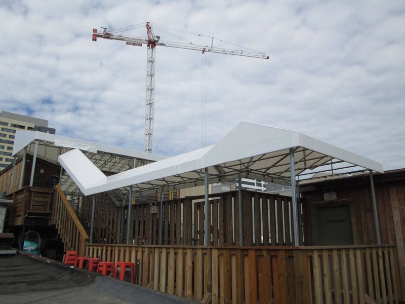 Outdoor deck with white canopy and crane in the background, cloudy sky.