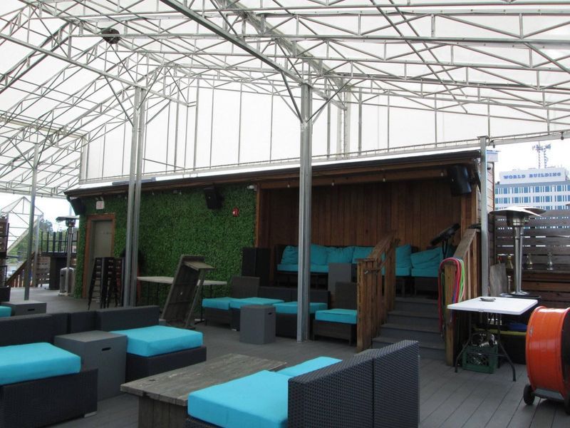 Rooftop bar with teal cushions, wooden structures, and a white canopy.