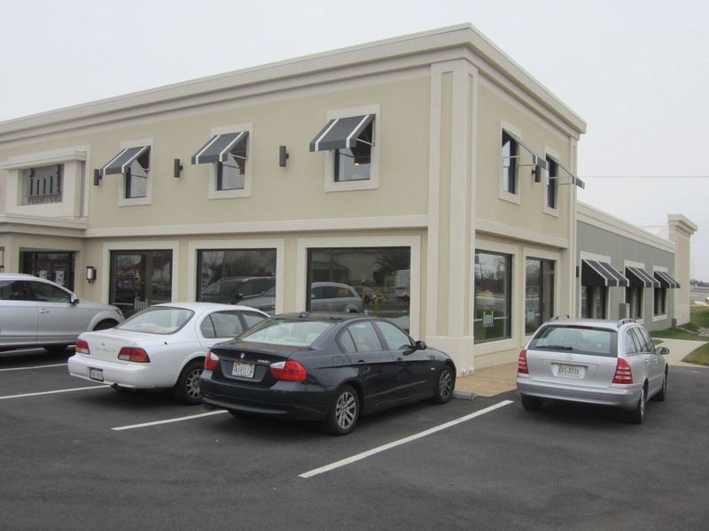 Exterior of a beige commercial building with awnings over windows; cars parked in front.