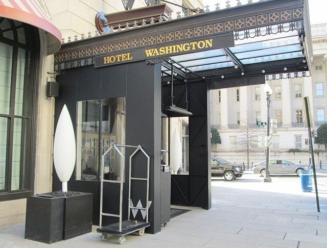 Hotel Washington entrance with black canopy, sign, and luggage cart on a sunny day.