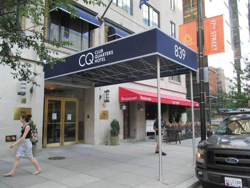 Entrance to Club Quarters hotel at 839 17th St. NW. Dark blue awning, red restaurant sign, woman walking, and parked truck.