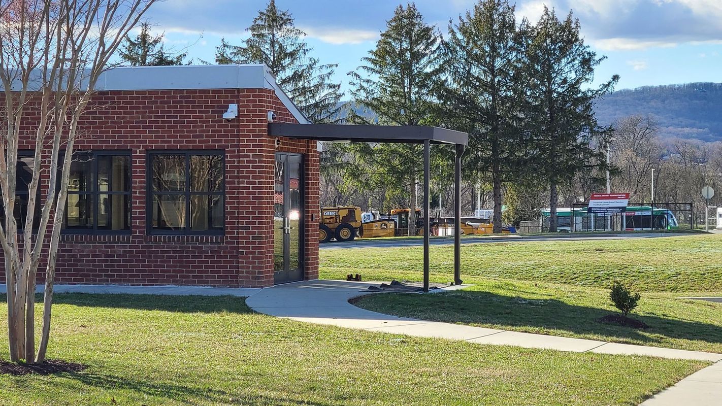 Brick building with awning, next to a grassy lawn. Construction equipment and trees in the background.