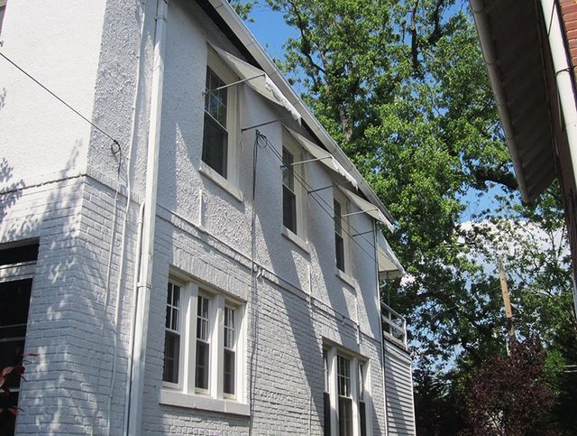 White-painted brick building with multiple windows; awnings provide shade. Tree in the background.