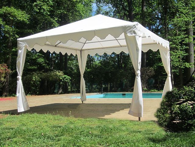 White gazebo with curtains near a pool, set on a sunny, grassy lawn.