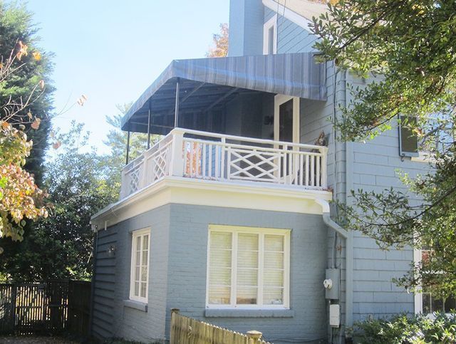 Blue house with a second-story balcony. White railing, blue awning, and brick facade.