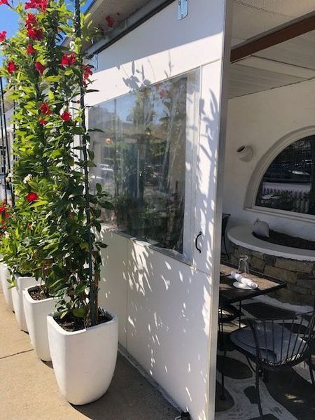 Outdoor restaurant seating with red flowering vines in white planters, next to a partially enclosed space with a table and chairs.