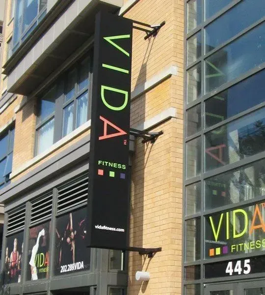 Black sign for VIDA Fitness hanging on a building. 