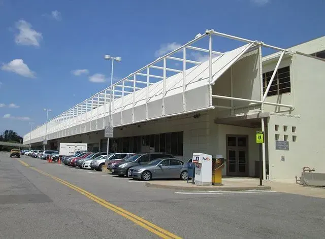 Cars parked outside a light-colored building with a long, white, metal awning. Blue sky.