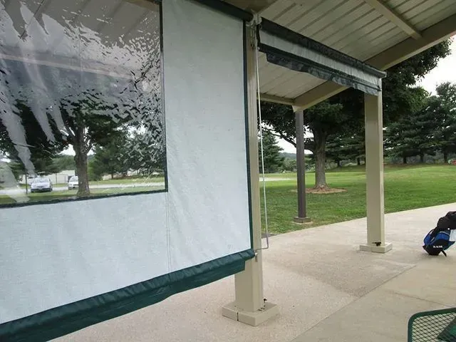 White and green awning with a clear window attached to a covered outdoor seating area.
