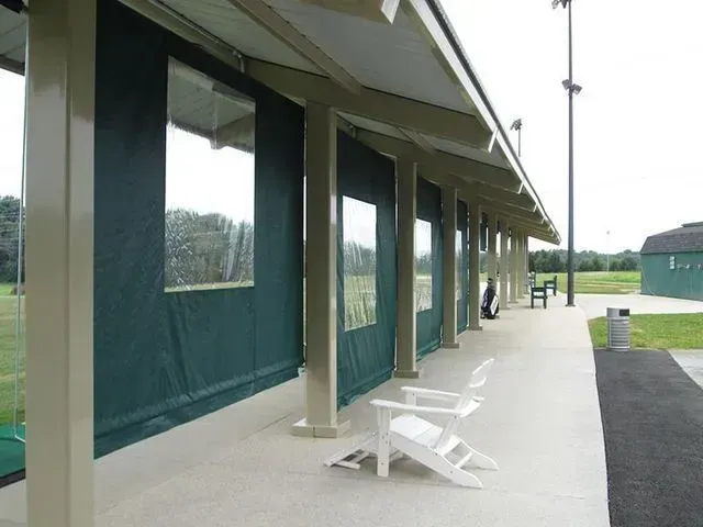 Golf driving range with green curtains, white chairs, and a concrete walkway.