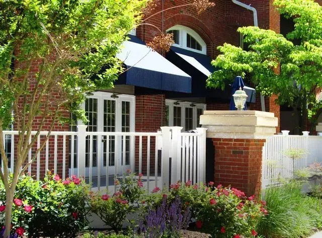 Brick building with white picket fence, awning, and landscaping.