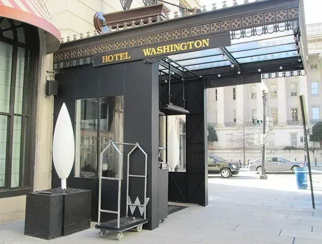Hotel Washington entrance with black awning, glass roof, and luggage cart, in Washington, DC.