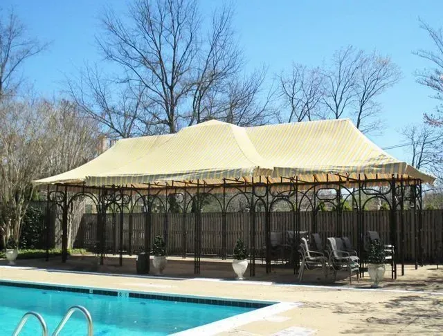 Poolside gazebo with a beige roof and black wrought iron framework; chairs are visible inside.