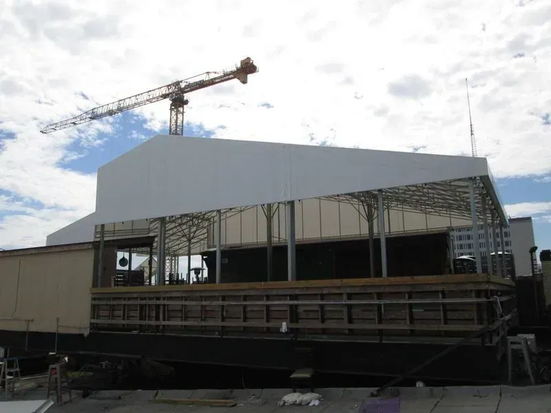 Construction site with crane; partially built structure with white roof, beige siding, and metal frame.
