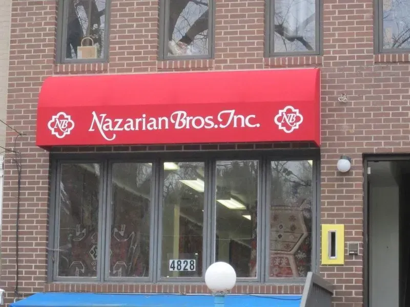 Red awning over Nazarian Bros. Inc. storefront with windows; brick building; white logo and text.