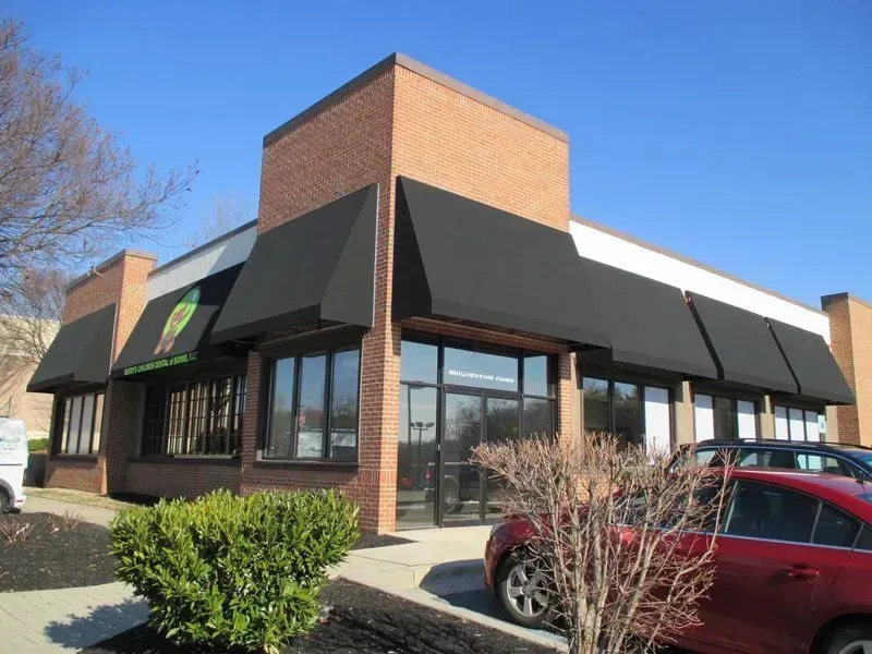 Brick building with black awnings, glass windows, and a shrub.
