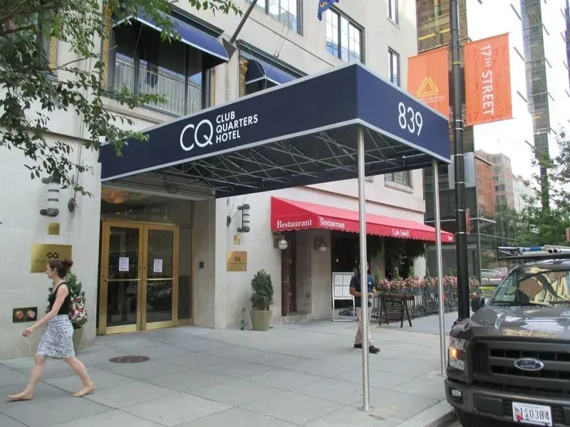 Entrance to Club Quarters hotel at 839, with a woman walking by. A restaurant is to the right.