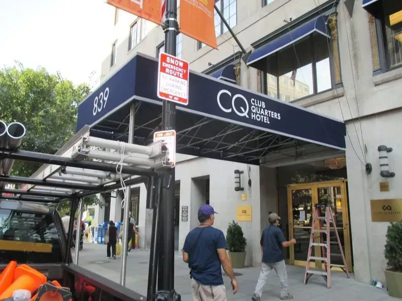 Workers near the entrance of the CQ Club Quarters Hotel with a dark blue awning over the entrance.
